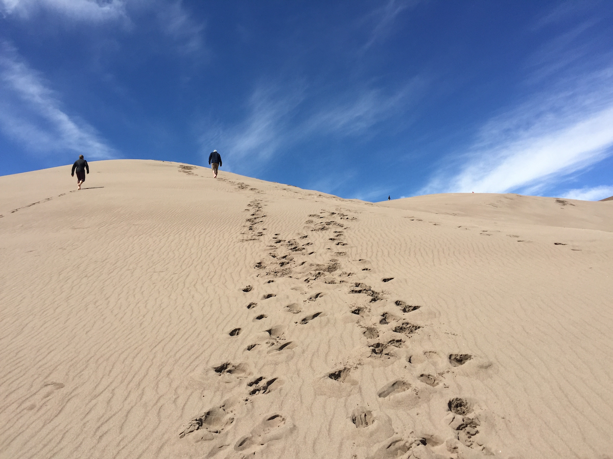 two people walking up a sand dune